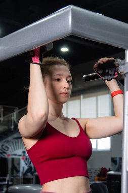 Spor salonundaki bir makinede barfiks çeken genç atletik kadın. Kol ve sırt egzersizi.