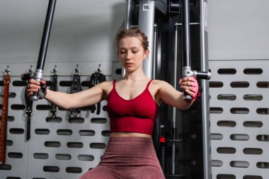 Genç atletik güzel bir kadın tam teçhizatlı bir spor salonunda göğüs makinesinde egzersiz yapıyor..