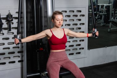 Genç atletik güzel bir kadın tam teçhizatlı bir spor salonunda göğüs makinesinde egzersiz yapıyor..