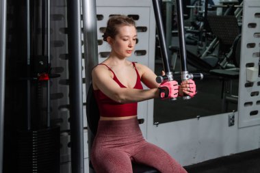 Genç atletik güzel bir kadın tam teçhizatlı bir spor salonunda göğüs makinesinde egzersiz yapıyor..