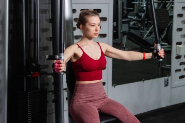 Genç atletik güzel bir kadın tam teçhizatlı bir spor salonunda göğüs makinesinde egzersiz yapıyor..