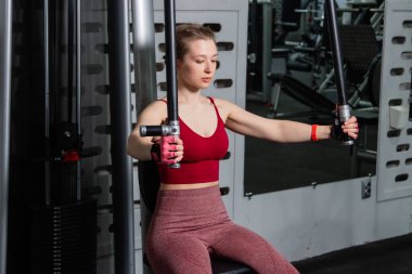 Genç atletik güzel bir kadın tam teçhizatlı bir spor salonunda göğüs makinesinde egzersiz yapıyor..