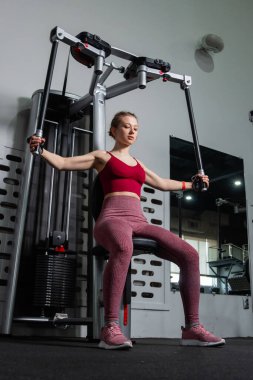 Genç atletik güzel bir kadın tam teçhizatlı bir spor salonunda göğüs makinesinde egzersiz yapıyor..