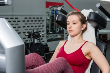 Genç, atletik bir kadın spor salonundaki bir makineye bacak presi yapıyor, bacaklarını çalıştırmak için..