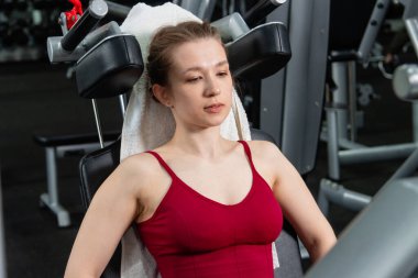 Genç, atletik bir kadın spor salonundaki bir makineye bacak presi yapıyor, bacaklarını çalıştırmak için..