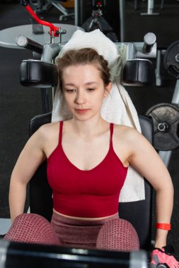 Genç, atletik bir kadın spor salonundaki bir makineye bacak presi yapıyor, bacaklarını çalıştırmak için..