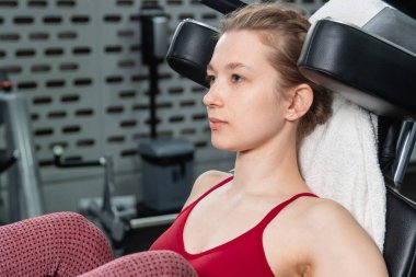 Genç, atletik bir kadın spor salonundaki bir makineye bacak presi yapıyor, bacaklarını çalıştırmak için..
