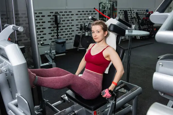 Genç, atletik bir kadın spor salonundaki bir makineye bacak presi yapıyor, bacaklarını çalıştırmak için..