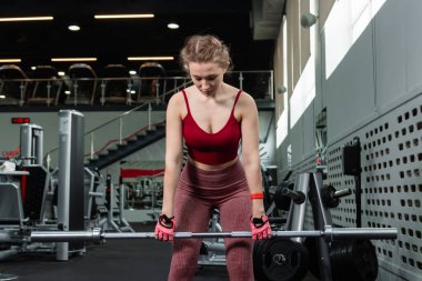 Genç bir atletik kadın spor salonunda halterle ağırlık kaldırma, sırt ve bacak antrenmanı yapıyor..