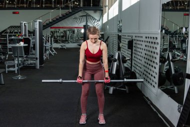 Genç bir atletik kadın spor salonunda halterle ağırlık kaldırma, sırt ve bacak antrenmanı yapıyor..