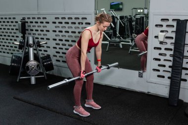 Genç bir atletik kadın spor salonunda halterle ağırlık kaldırma, sırt ve bacak antrenmanı yapıyor..