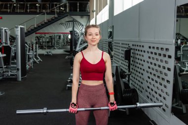 Genç bir atletik kadın spor salonunda halterle ağırlık kaldırma, sırt ve bacak antrenmanı yapıyor..