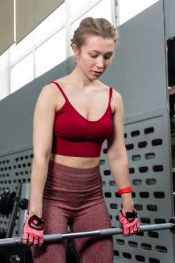 Genç bir atletik kadın spor salonunda halterle ağırlık kaldırma, sırt ve bacak antrenmanı yapıyor..