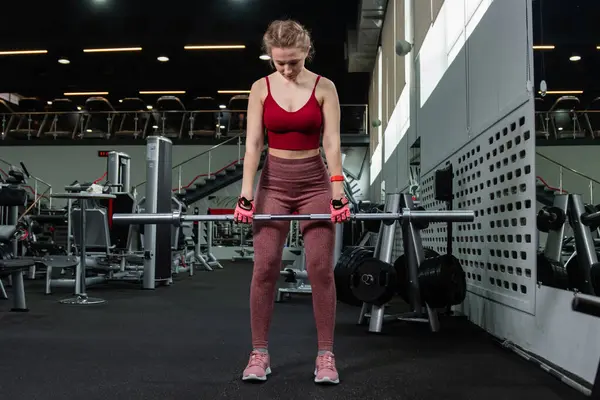 Genç bir atletik kadın spor salonunda halterle ağırlık kaldırma, sırt ve bacak antrenmanı yapıyor..