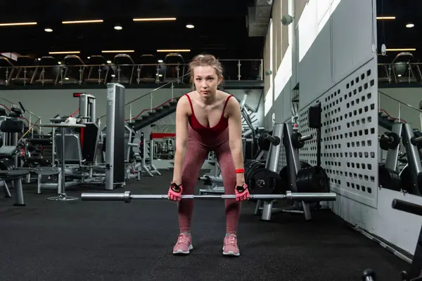 Genç bir atletik kadın spor salonunda halterle ağırlık kaldırma, sırt ve bacak antrenmanı yapıyor..