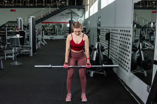 Genç bir atletik kadın spor salonunda halterle ağırlık kaldırma, sırt ve bacak antrenmanı yapıyor..