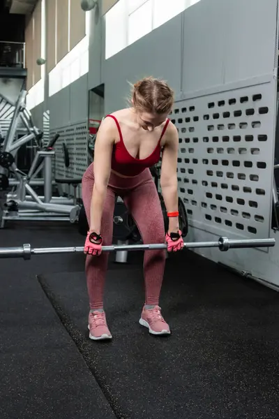 Genç bir atletik kadın spor salonunda halterle ağırlık kaldırma, sırt ve bacak antrenmanı yapıyor..