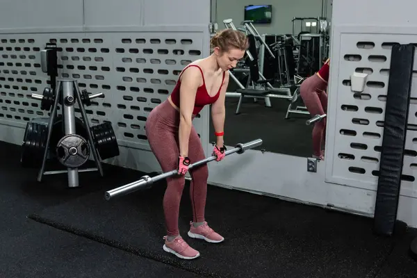 Genç bir atletik kadın spor salonunda halterle ağırlık kaldırma, sırt ve bacak antrenmanı yapıyor..