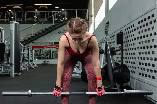 Genç bir atletik kadın spor salonunda halterle ağırlık kaldırma, sırt ve bacak antrenmanı yapıyor..