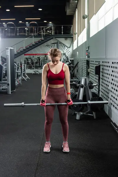 Genç bir atletik kadın spor salonunda halterle ağırlık kaldırma, sırt ve bacak antrenmanı yapıyor..