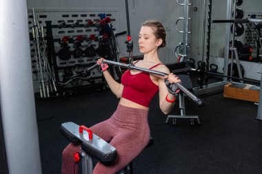 Spor salonundaki bir çekme makinesinde egzersiz yapan atletik genç bir kadın. Vücut ve kol egzersizi.