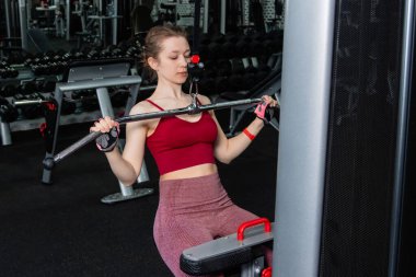 Spor salonundaki bir çekme makinesinde egzersiz yapan atletik genç bir kadın. Vücut ve kol egzersizi.