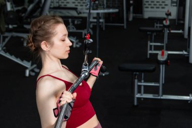 Spor salonundaki bir çekme makinesinde egzersiz yapan atletik genç bir kadın. Vücut ve kol egzersizi.