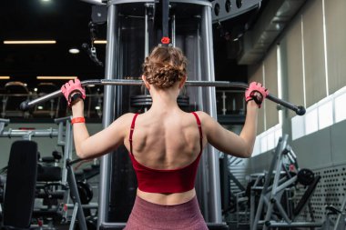 Spor salonundaki bir çekme makinesinde egzersiz yapan atletik genç bir kadın. Vücut ve kol egzersizi.
