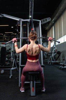 Spor salonundaki bir çekme makinesinde egzersiz yapan atletik genç bir kadın. Vücut ve kol egzersizi.