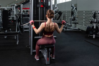 Spor salonundaki bir çekme makinesinde egzersiz yapan atletik genç bir kadın. Vücut ve kol egzersizi.