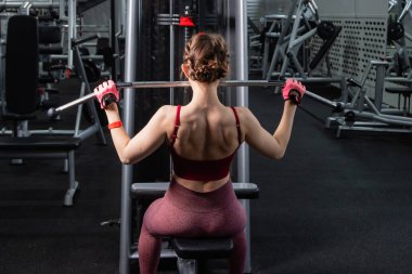 Spor salonundaki bir çekme makinesinde egzersiz yapan atletik genç bir kadın. Vücut ve kol egzersizi.