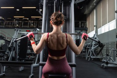 Spor salonundaki bir çekme makinesinde egzersiz yapan atletik genç bir kadın. Vücut ve kol egzersizi.