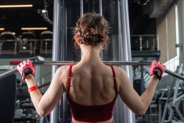 Spor salonundaki bir çekme makinesinde egzersiz yapan atletik genç bir kadın. Vücut ve kol egzersizi.