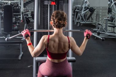 Spor salonundaki bir çekme makinesinde egzersiz yapan atletik genç bir kadın. Vücut ve kol egzersizi.