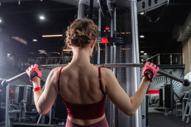 Spor salonundaki bir çekme makinesinde egzersiz yapan atletik genç bir kadın. Vücut ve kol egzersizi.