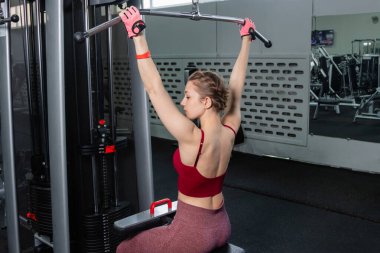 Spor salonundaki bir çekme makinesinde egzersiz yapan atletik genç bir kadın. Vücut ve kol egzersizi.