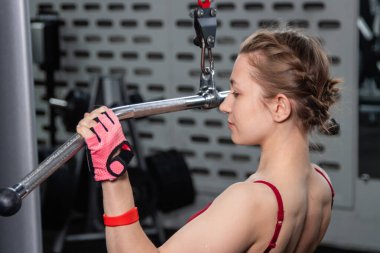 Spor salonundaki bir çekme makinesinde egzersiz yapan atletik genç bir kadın. Vücut ve kol egzersizi.