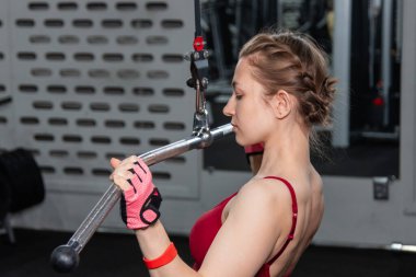 Spor salonundaki bir çekme makinesinde egzersiz yapan atletik genç bir kadın. Vücut ve kol egzersizi.