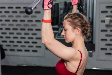 Spor salonundaki bir çekme makinesinde egzersiz yapan atletik genç bir kadın. Vücut ve kol egzersizi.