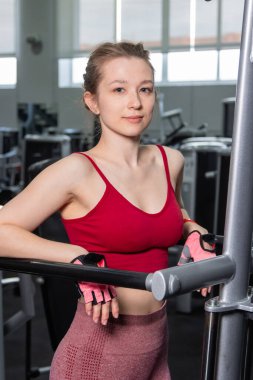 Egzersiz makinesinin yanında duran genç atletik kadın, triseps egzersizi yapıyor, spor salonunda paralel bar şınav çekiyor..