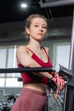 Egzersiz makinesinin yanında duran genç atletik kadın, triseps egzersizi yapıyor, spor salonunda paralel bar şınav çekiyor..