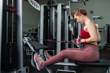 Sporcu genç bir kadın spor salonundaki bir makinede onu eğitmek için egzersiz yapıyor..