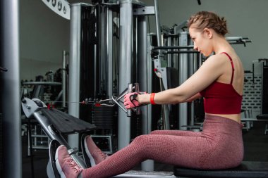 Sporcu genç bir kadın spor salonundaki bir makinede onu eğitmek için egzersiz yapıyor..