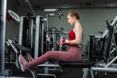 Sporcu genç bir kadın spor salonundaki bir makinede onu eğitmek için egzersiz yapıyor..