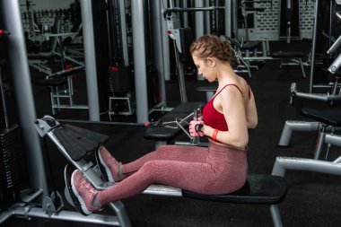 Sporcu genç bir kadın spor salonundaki bir makinede onu eğitmek için egzersiz yapıyor..