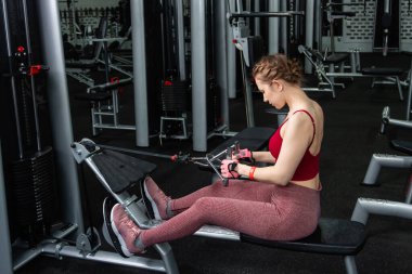 Sporcu genç bir kadın spor salonundaki bir makinede onu eğitmek için egzersiz yapıyor..