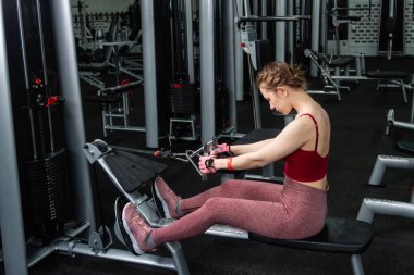 Sporcu genç bir kadın spor salonundaki bir makinede onu eğitmek için egzersiz yapıyor..