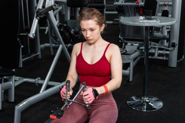 Sporcu genç bir kadın spor salonundaki bir makinede onu eğitmek için egzersiz yapıyor..