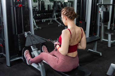 Sporcu genç bir kadın spor salonundaki bir makinede onu eğitmek için egzersiz yapıyor..