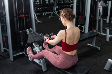 Sporcu genç bir kadın spor salonundaki bir makinede onu eğitmek için egzersiz yapıyor..